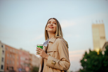 A woman is enjoying city life while having her coffee to go on a street.