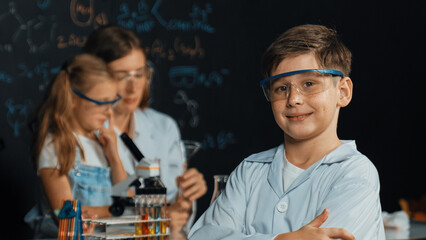 Smart boy pour chemical liquid in beaker while teacher giving advice at STEM science class. Student...