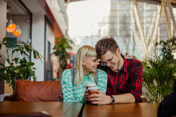 Couple in love is sitting at train station in cafe and hugging.