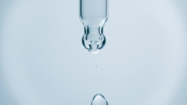 Cosmetics blue liquid dripping from laboratory glass pipette in super slow motion. Macro shot of drop hanging down from chemical dropper. Abstract body care serum ingredients formulating concept
