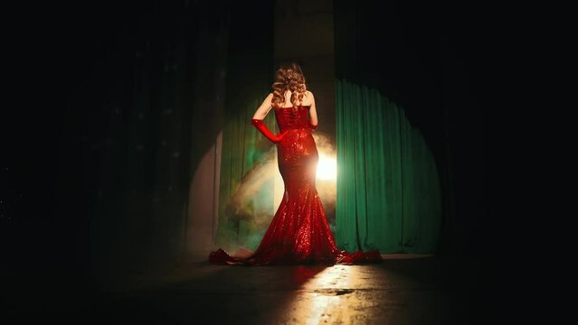 portrait back rear view Sexy beauty woman stands on stage concert hall singer performing song holding retro microphone in hands. happy girl sings in dark karaoke bar clud makeup red lips dress. art 4k