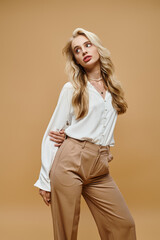 sensual blonde woman in old money style attire looking away on beige backdrop, classic fashion shoot