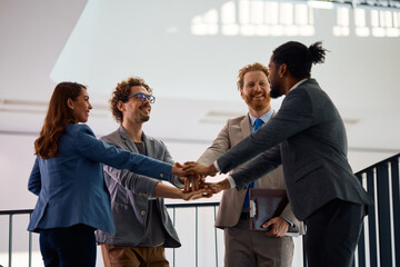 Happy multiracial business team gathering their hands in unity in office.