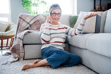 Obraz premium Full size portrait of pretty barefoot lady sit carpet floor speak telephone netbook sofa modern apartment inside