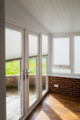 Made to measure blinds on windows and doors in a white conservatory with wooden floor and red brick...