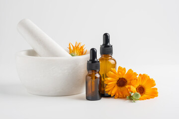 Calendula flowers in mortar and amber glass dropping bottles with essential oil. Marigold medicinal...