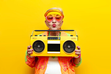 funny crazy granny in hipster clothes listening to music on a tape recorder and showing a kiss on a...