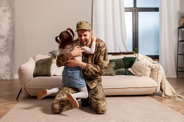 happy Ukrainian army soldier in camouflage uniform returned home and meets his daughter, the child...