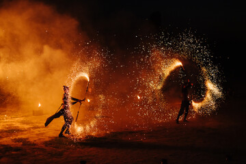 People dance a passionate dance with a fiery spinning wheel in hand. Tribal dancer. Fire show. Spin fire around a swing on the beach in a full moon. The fire shows many sparks at night - Powered by Adobe