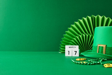 St. Patrick's Day revelry: a touch of emerald charm. Side view of green hat, calendar set to March 17th, green paper fan decoration, gold coins on green background with space for festive announcements - obrazy, fototapety, plakaty