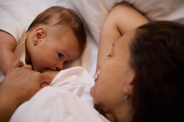 Authentic portrait of a newborn baby boy sucking milk from mothers breast. Portrait of mom and breastfeeding baby.