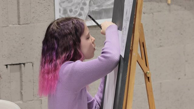 Cute girl with pink hair painting on canvas, holding pencil, enjoying creative hobby, childhood, training artistic skills.