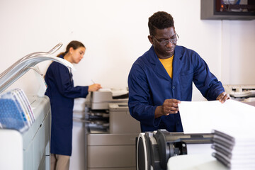 Printing house employee works on modern printing equipment