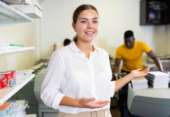Happy young woman in white shirt sticking out her left hand to show the workflow in the printing...