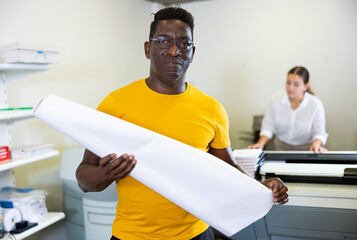 Middle-aged African American male specialist holding large format paper whatman in a roll in the...