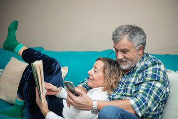 elderly couple on sofa reading book and using smartphone