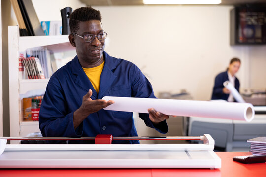 Middle-aged African American male specialist in uniform holding whatman in a roll in the middle of print shop