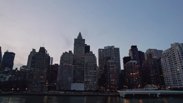 Dusk blue hour pov perspective of midtown Manhattan in NYC New York City from east river ferry, with a view of skyscrapers, business, traffic, office buildings, towers, and night life