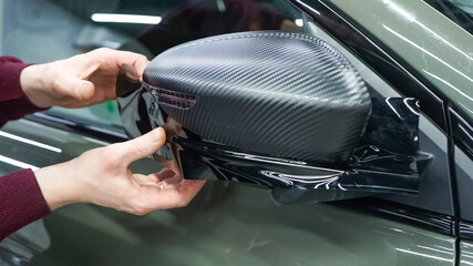 A car wrapping specialist applies a polyurethane film to the car. Selective focus. PPF protective film. The process of installing PPF on the side mirror. Car wrapping close-up.
