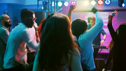 Group of friends enjoying party at club, dancing on modern music and jumping on dance floor. Young people feeling happy and showing cool moves at discotheque, clubbing. Handheld shot.