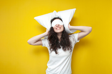 young girl in sleep mask and pajamas sleeps hugging pillow on yellow background, healthy sleep...