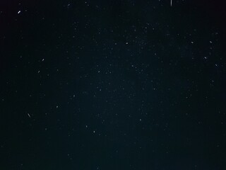 Starry night sky in village. A black-gray night sky in which white spots of distant stars are visible. Gray clouds float across the sky, covering some of the stars. Stars can be seen across the sky.