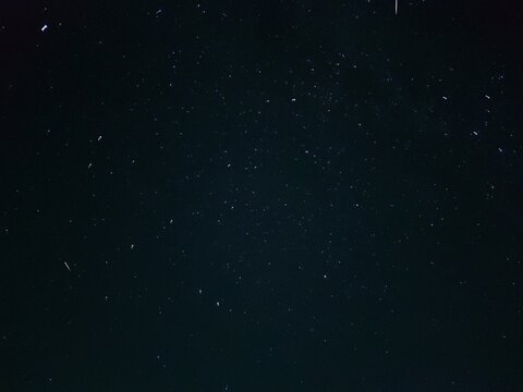 Starry night sky in village. A black-gray night sky in which white spots of distant stars are visible. Gray clouds float across the sky, covering some of the stars. Stars can be seen across the sky.