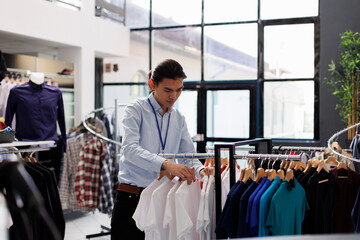 Asian employee arranging casual wear items in shopping centre, preparing store for opening. Stylish...