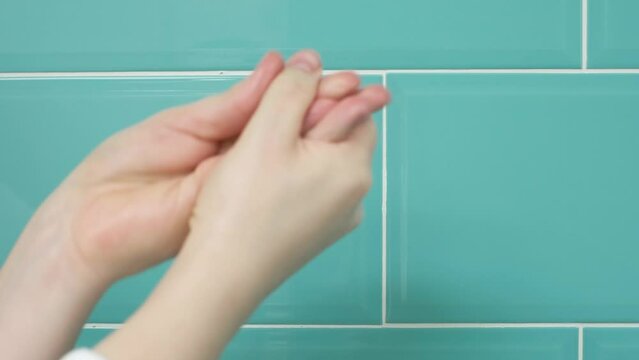 Moisturizing cream on female hand against background of mint tiles side view, skin care concept.