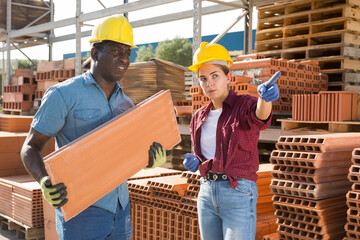 Attractive female manager pointing to african male worker where to carry bricks in a building...