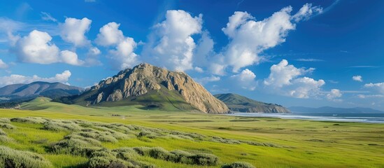 A scenic view from Highway on the Big Sur coast near Cambria CA showcases a grassy field with a mountain in the background, along with Morro Rock, Morro Bay, Montana de Oro, rural coastal hills, and - obrazy, fototapety, plakaty