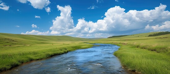 A flowing river cuts through a vibrant green field under a cloudy blue sky in a scenic summer landscape.