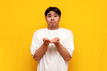 sad asian young man in white t-shirt begging over yellow isolated background