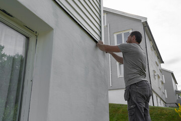 Man Finishing Applying Masking Tape on House: Precision in Home Improvement.