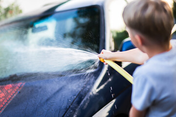 A child washes the window of a car with water from a garden hose