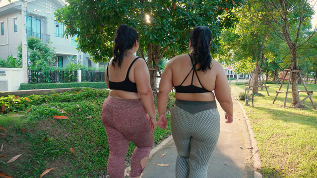 Two asian woman fat in sportswear jogging together on pathway at park, woman and friends obesity doing activity with cardio or walking, workout and exercise, plus size and health for weightloss.