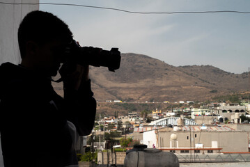 Hombre a contraluz, espiando casas con camara fotografica con lente 150mm.