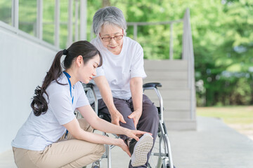 老人ホームで車椅子に乗りながらリハビリする高齢者と介護士（膝・膝痛）
