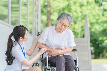 お腹をおさえる車椅子に乗った高齢者と介護士（胃潰瘍・胃炎・胃痛）
