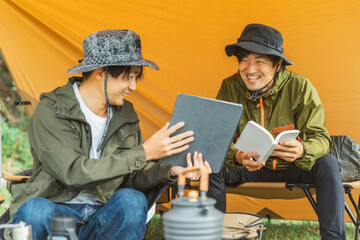 秋冬のキャンプ場でテントを張って読書をする男性キャンパー
