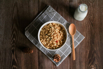Granola breakfast with raisins, cranberries and hazelnuts served with milk in white bowl on wooden table. Healthy eating.  