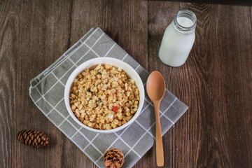 Granola breakfast with raisins, cranberries and hazelnuts served with milk in white bowl on wooden table. Healthy eating.  