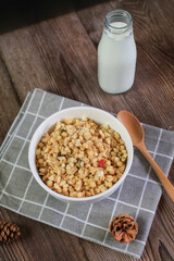 Granola breakfast with raisins, cranberries and hazelnuts served with milk in white bowl on wooden table. Healthy eating.  