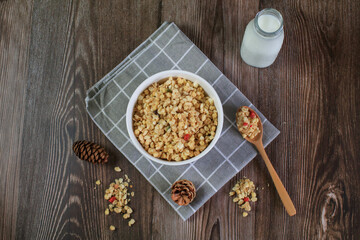 Granola breakfast with raisins, cranberries and hazelnuts served with milk in white bowl on wooden table. Healthy eating.  