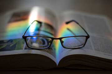 Libro de Biologia abierto de frente, con lentes de lectura enmedio, y un rayo de luz multicolor...