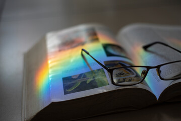Libro de Biologia abierto, con lentes de lectura enmedio, y un rayo de luz multicolor desbordandose...