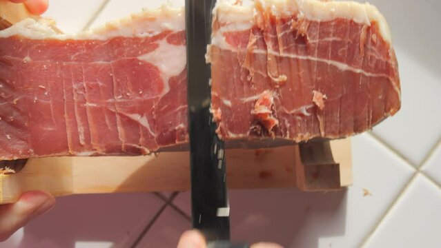 Spanish traditional pork jamon. A knife cuts a piece of hamon meat into thin slices in the kitchen, top view