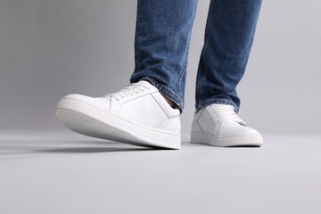 Man wearing stylish white sneakers on grey background, closeup - Powered by Adobe