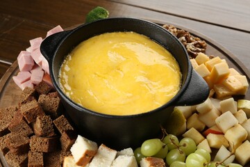 Fondue pot with melted cheese and different products on wooden table, closeup