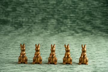 Row of decorative gold bunnies on a textured green velvet background, Happy Easter
